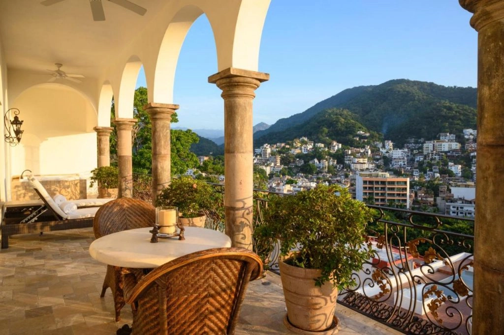 View of Casa Kimberly, Puerto Vallarta's luxurious boutique hotel, showcasing its iconic white façade, arched doorways, all set against a backdrop of lush green hills and vibrant blue skies