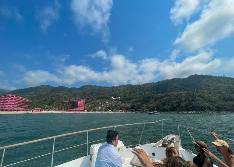 A group of people on a boat enjoying day trips from Puerto Vallarta in front of a pink building.