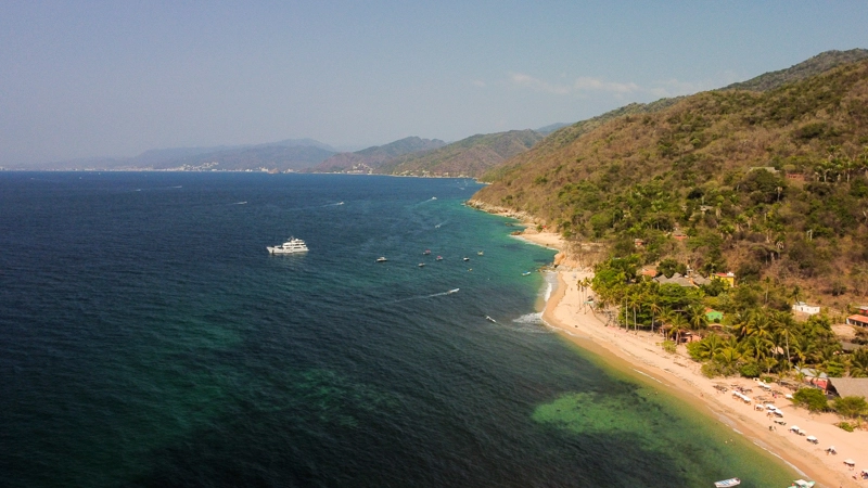 Aerial view of one of the best beaches in Puerto Vallarta, featuring clear blue water, boats, and a lush green hillside.