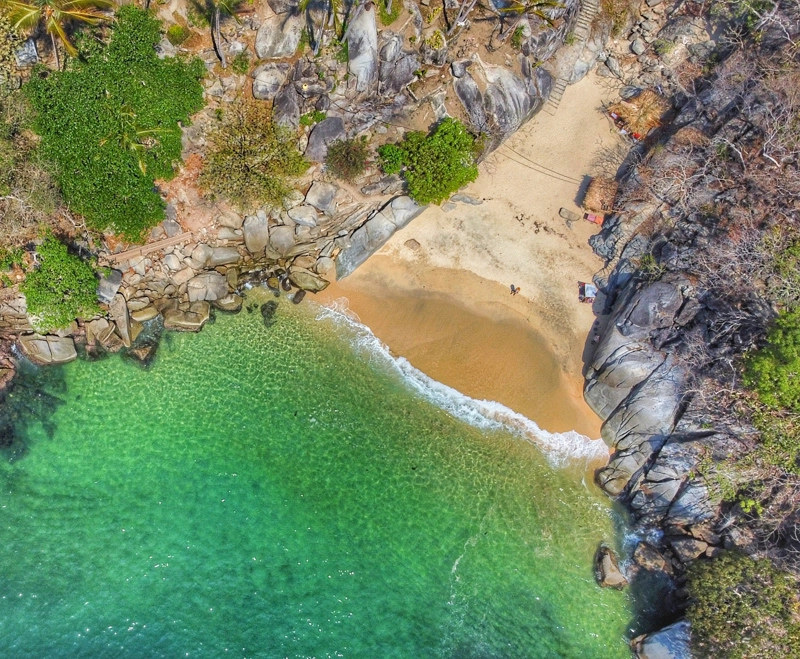 aerial view of an a beach in a secluded cove. emerald greenw ater with gentle waves against the brown sand. lora is standing by herself. Playa Colomitos mexico