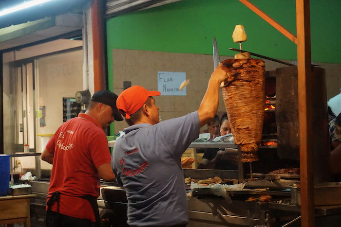 a mexican man with a knife carving meat for an al pastor taco