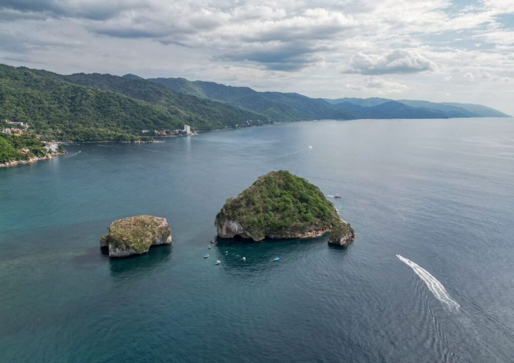 drone shot of los arcos marine parm from above. a boat goes past the islands with the backdrop of mountains.