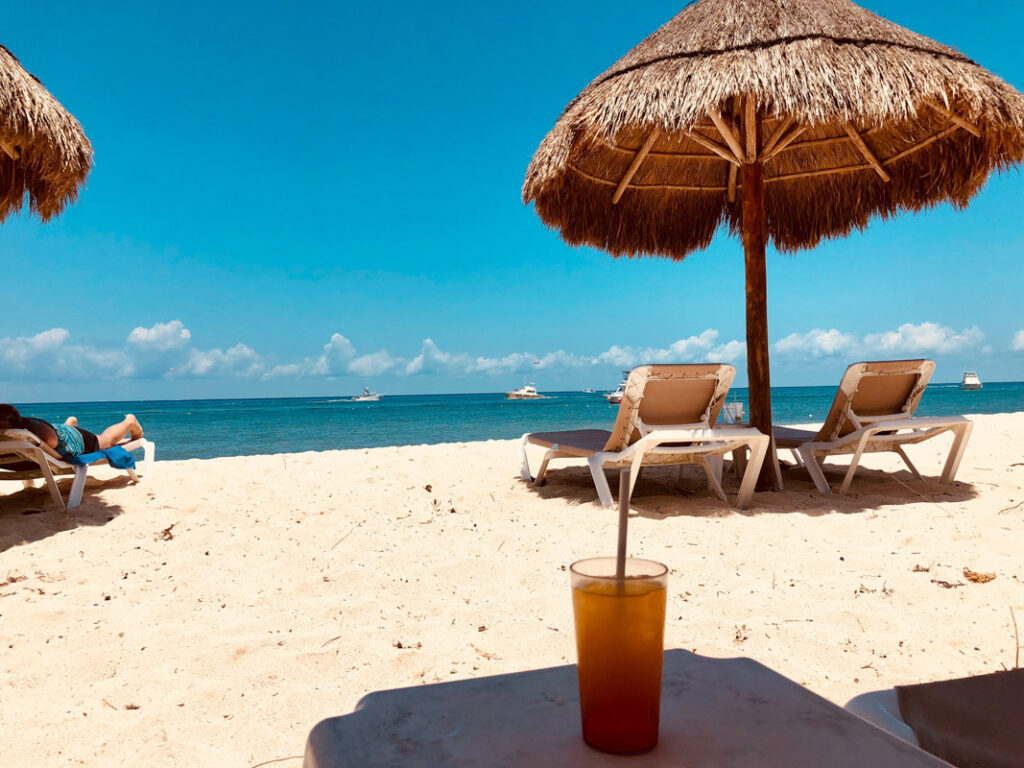 beach chairs under a hut facing the ocean on a beach in cozumel