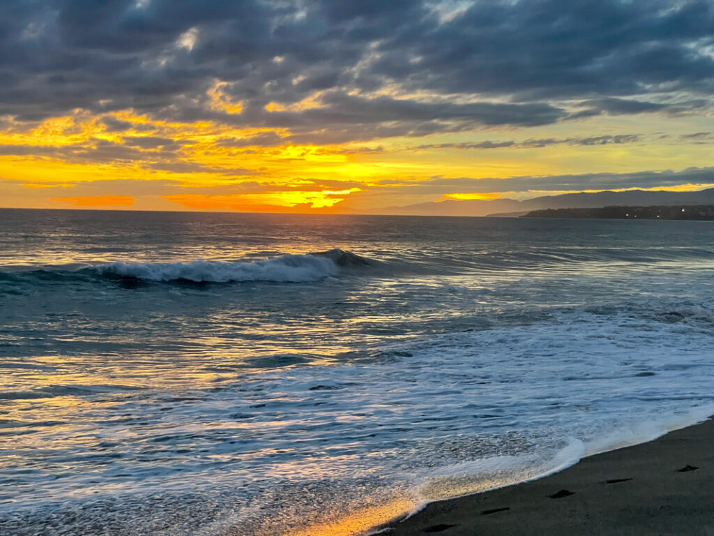 Captivating sunset over the beach in Puerto Escondido, Mexico, casting a warm golden glow across the sky and reflecting on the tranquil ocean waves, creating a serene and picturesque coastal scene.