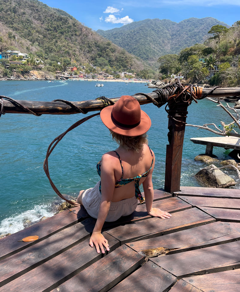 lora wearing a hat sitting facing the ocean while hiking the boca to las animas hike