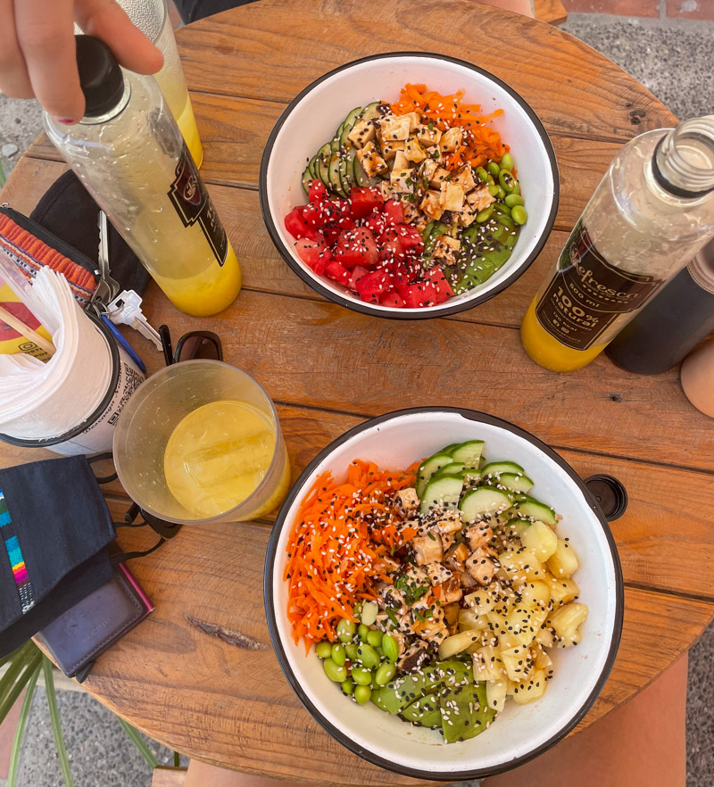 a bright poke poke bowl with a mango juice next to it.