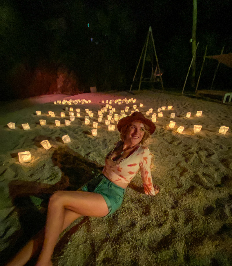 Lora sitting on a beach at night with lights around her