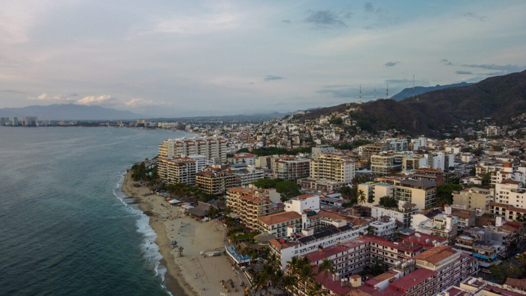 Picture of a vibrant beach town in Mexico, with crystal-clear turquoise waters, palm trees swaying in the breeze, and colorful houses dotting the sandy shore.