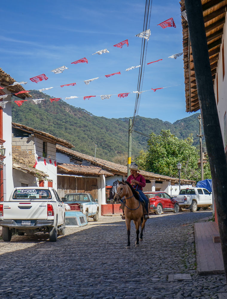man riding a horse through cobblestone streets with mountains in background