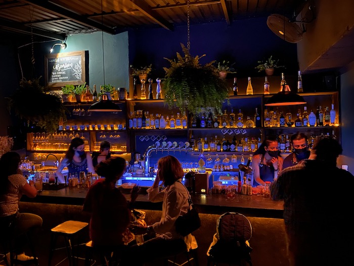 people sitting at the bar in El Colibri Puerto Vallarta. It is dimly literally  and a selection of alcohol is behind the bar.