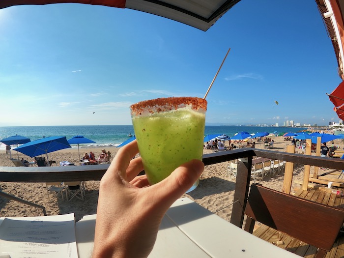 hand holding a Mezcal Cocktail on a bright sunny day by the beach