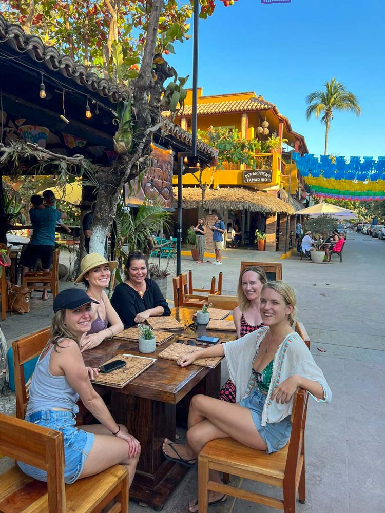 group of five girlfriends eating outdoors at a restaurant in san pancho. they are smiling looking a at the camera.