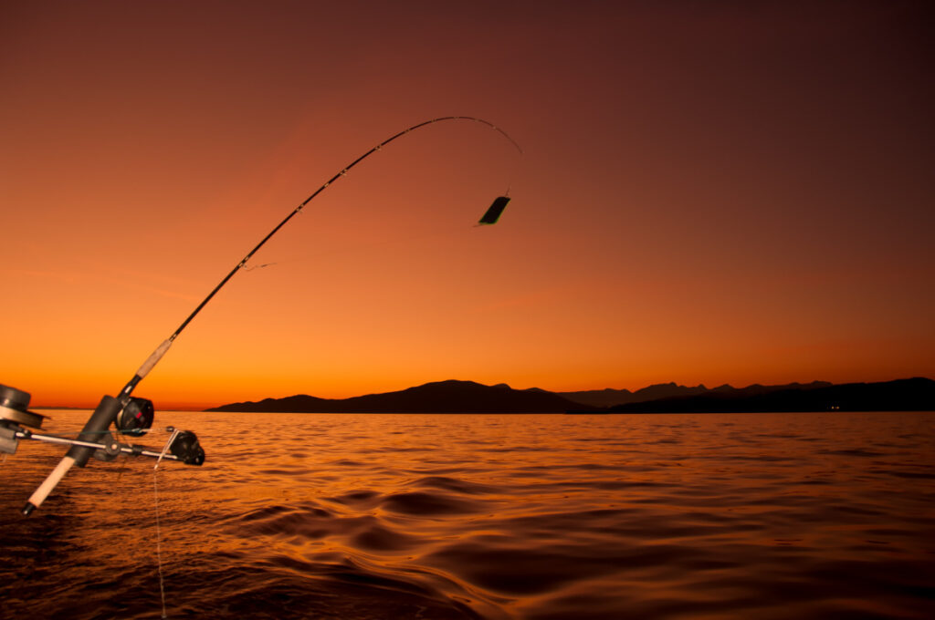 casting a fishing rod into the ocean while the sky is lit by a fiery orange and red sunset