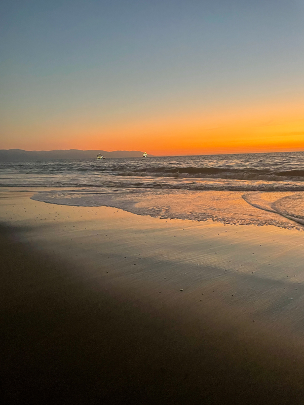 yellow and orange sunset over the pacific ocean. waves crashing into the beach with mountains in backdrop.