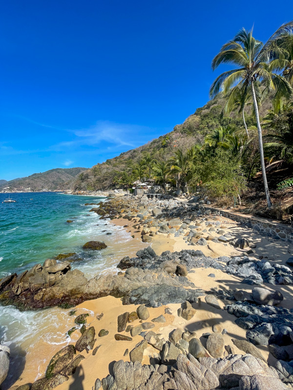 rocks dot the sandy shore of playa cabolla. swaying palm trees above the turquoise water create a perfect tropical scene.