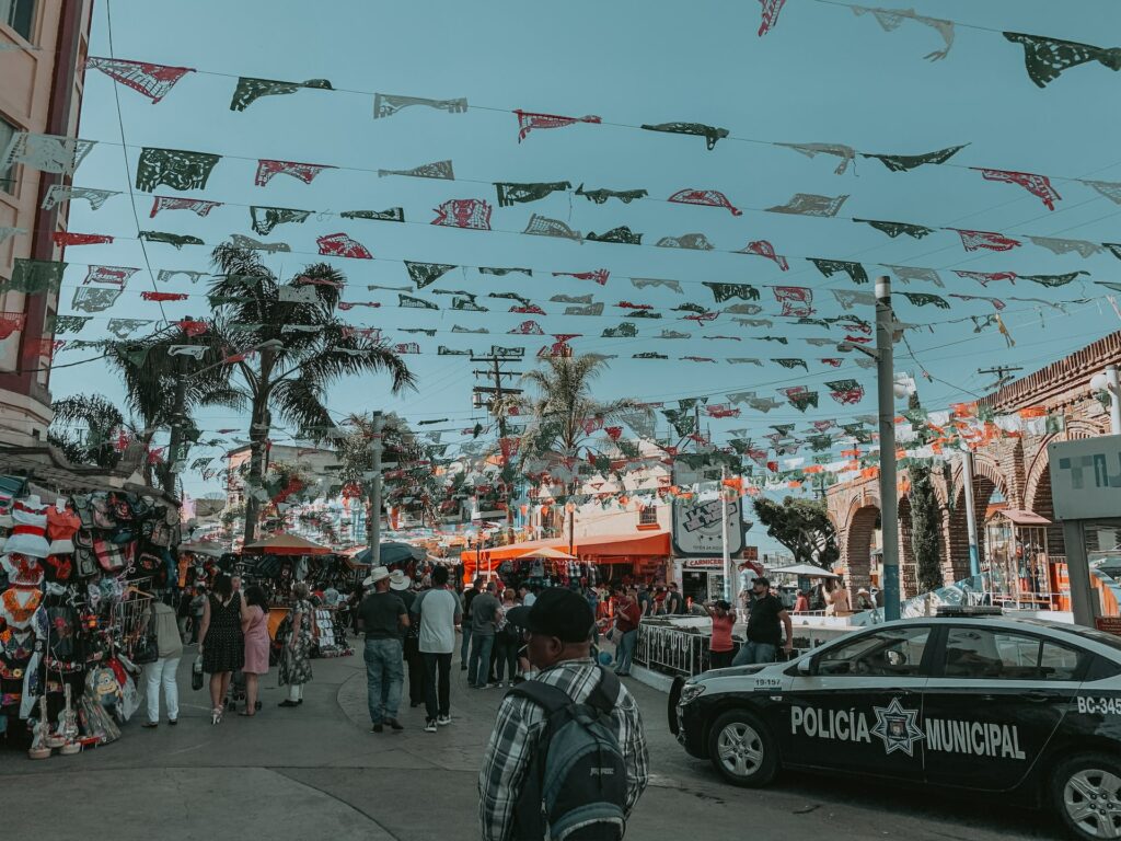 Image of a lively street in Tijuana, Mexico, bustling with activity, vibrant storefronts, street vendors, and a mix of pedestrians and vehicles, showcasing the energetic and diverse ambiance of the city.