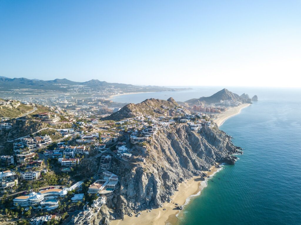 Scenic landscape in Cabo San Lucas, Mexico, showcasing dramatic rock formations against the backdrop of a deep blue sea, with golden sand beaches and a clear sky, offering a captivating blend of natural beauty and coastal charm