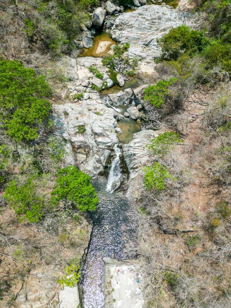 aerial photo showing quimixto waterfall from above. it is surrounded by lush jungle.