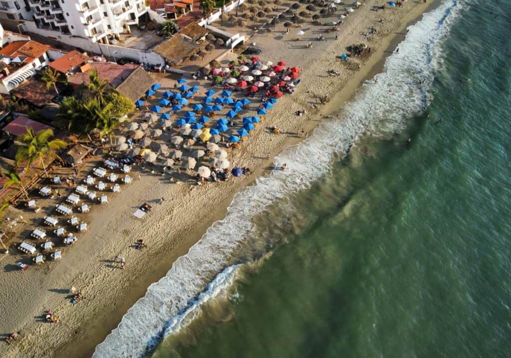 aerial view of los muertos beach puerto vallarta. waves crashing against the sand with beach umbrellas.
