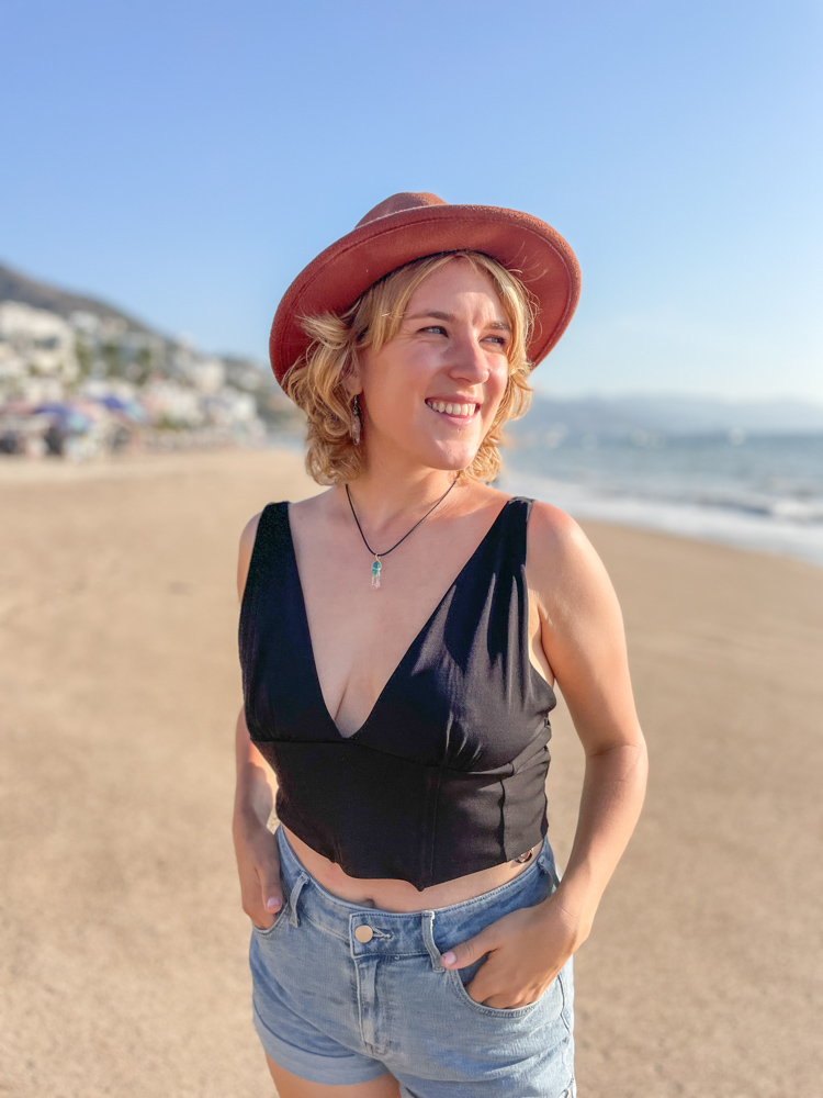 photo of lora pope on the beach in puerto vallarta wearing a black shirt and hat smiling into the distance