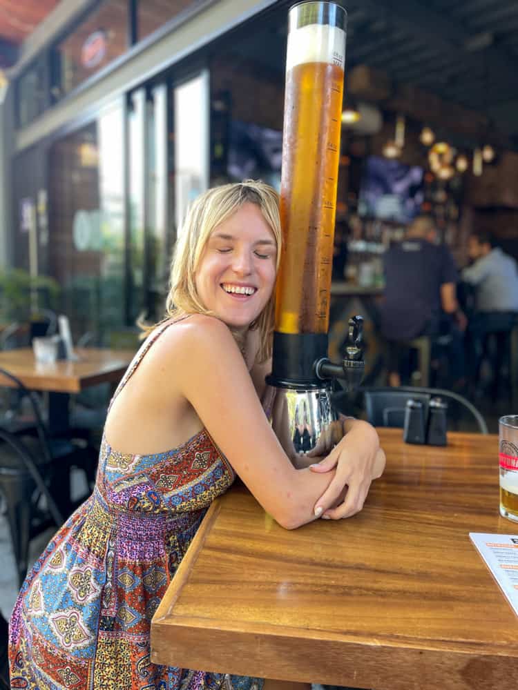 Lora with a smile hugging a large beer, enjoying the vibrant atmosphere of a lively brewhouse in versalles puerto vallarta