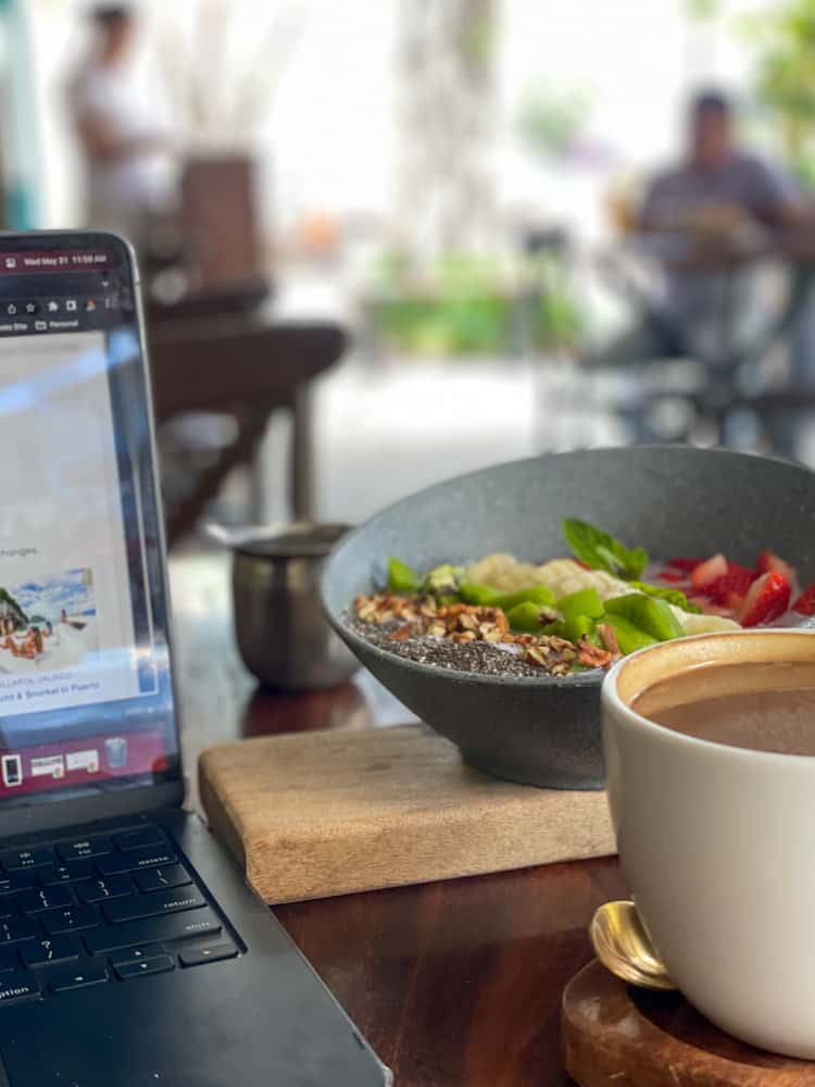 A laptop sits next to a beautifully presented cup of coffee and an acai bowl, creating a perfect workspace at Natureza coffee shop in Puerto Vallarta.