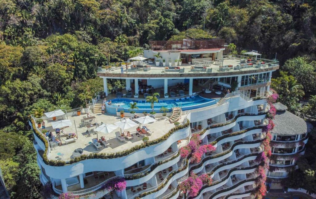 drone shot of the grand miramar puerto vallarta. you can see the rooftop pool and the hotel nestled in the mountains.
