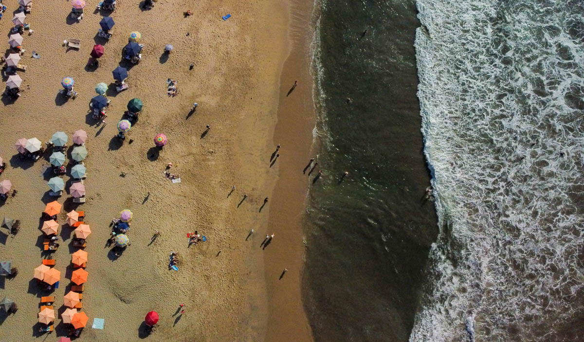 aerial photo of beach in san pancho mexico. half is ocean and half is golden sand beach with umbrellas.