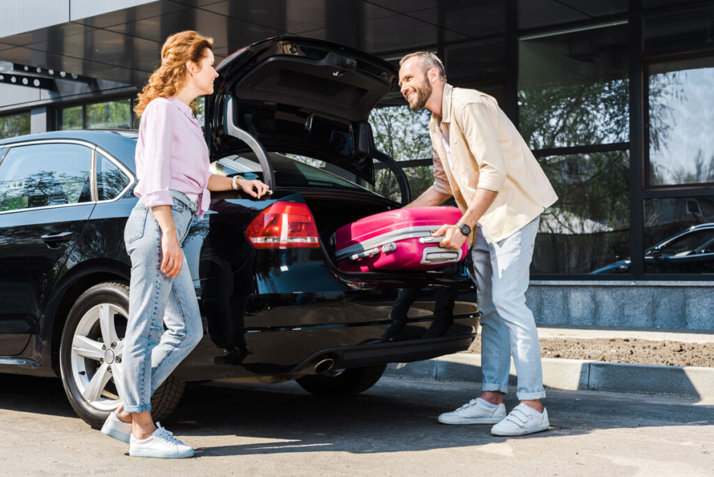 man putting luggage into rental car