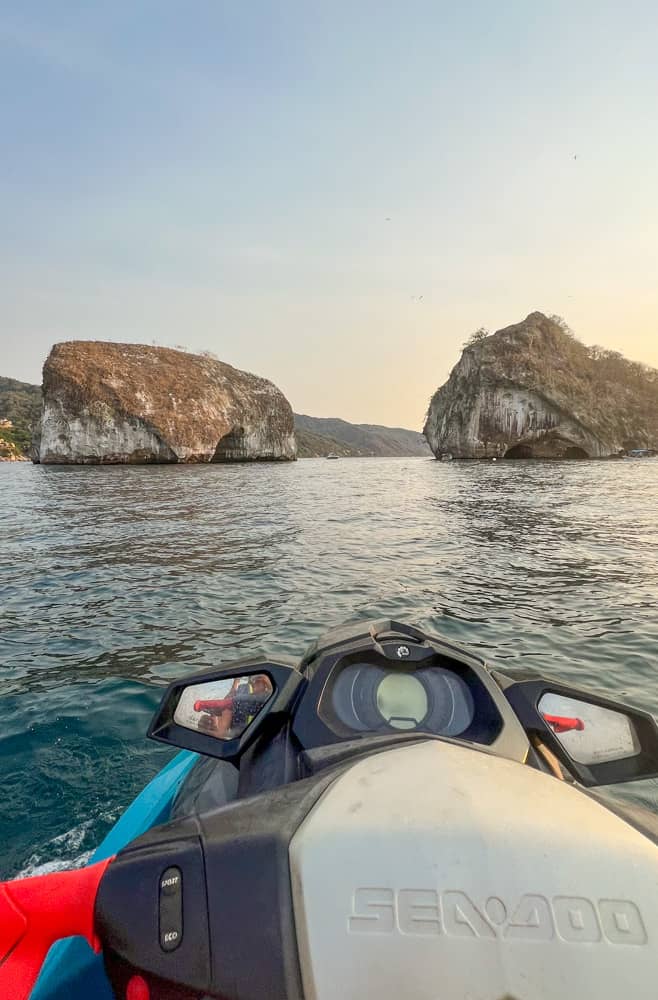 Jet ski gliding through the water with Los Arcos rock formation in the background.
