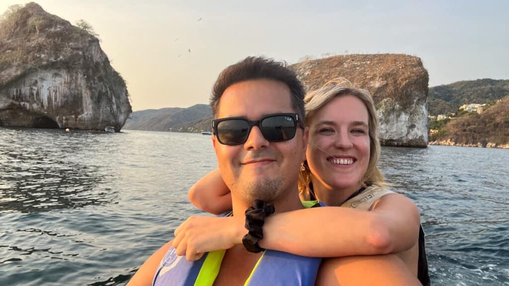 Two people on a jet ski capturing a selfie with the iconic Los Arcos rock formation as the backdrop.