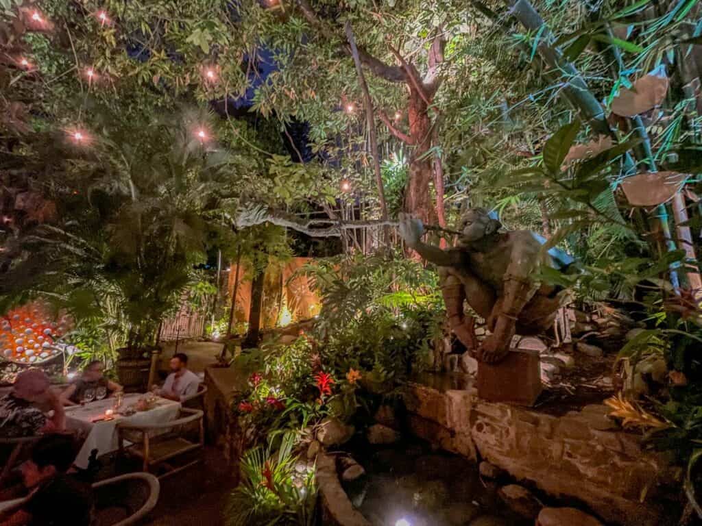 interior of cafes des artistes in puerto vallarta. lush green plants surround the restaurant tables creating a romantic setting.