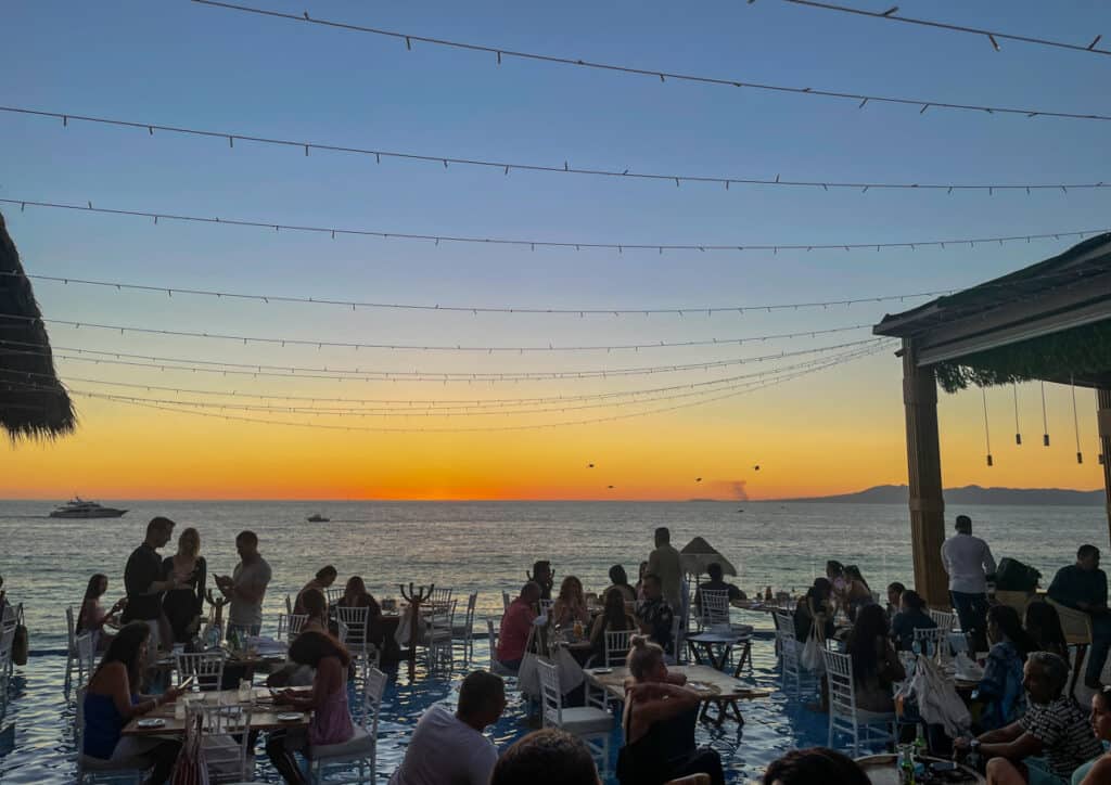 people dining at mar y vino, tables are in the pool with a view of the ocean and sun set from behind