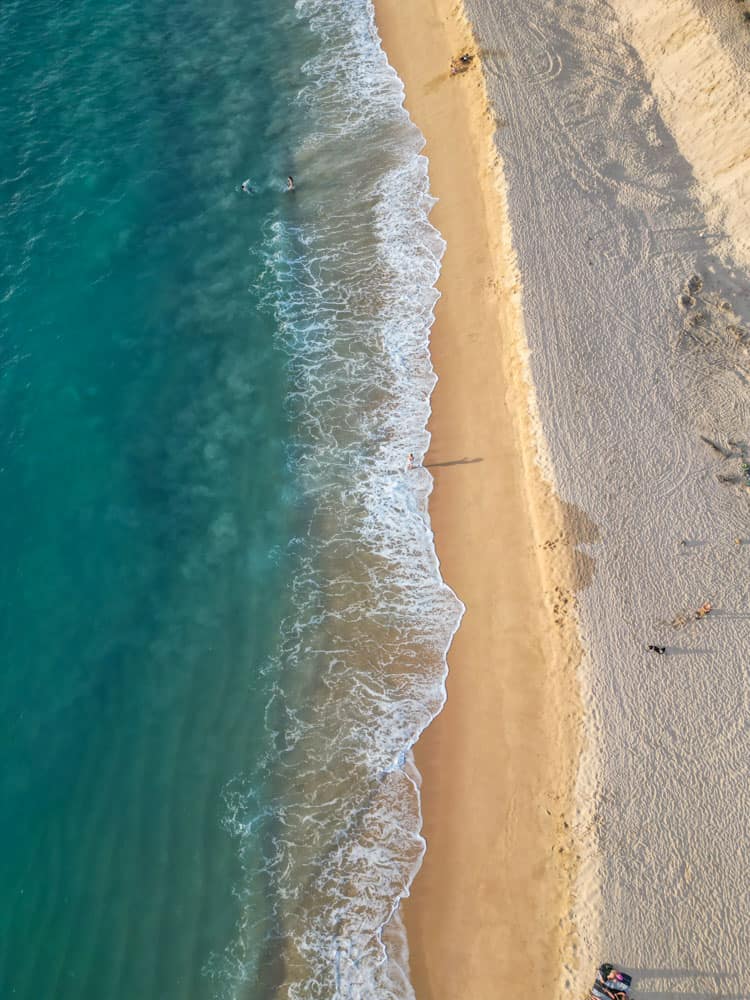 aerial photo of playa photo. half is turquoise ocean and half is golden sand beach. lora is walking alone on it.