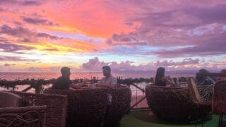 people dining at ik mixology bar on bamboo chairs while a pink and purple sun set paints the sky