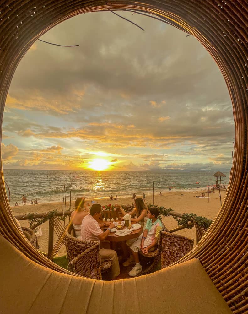 view of people dining on the beach in puerto vallarta with the sun setting in the backdrop