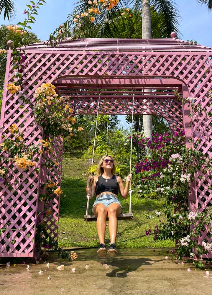 A woman swinging on a pink swing in a garden, an ideal Puerto Vallarta Instagram spot.