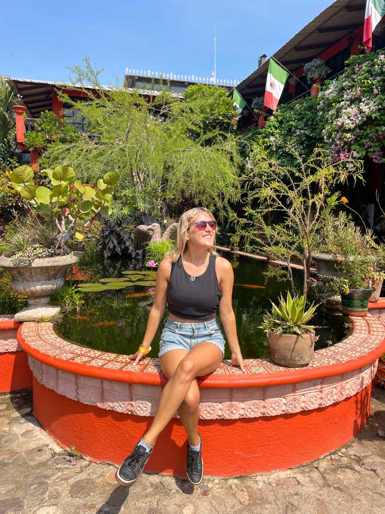 A woman sitting on a ledge in front of a pond at one of the stunning Puerto Vallarta Instagram spots.