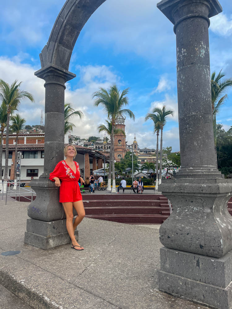A woman in a red dress posing in front of an arch at Puerto Vallarta, a popular Instagram spot.