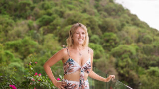 A woman in a floral romper standing on a balcony overlooking the mountains.