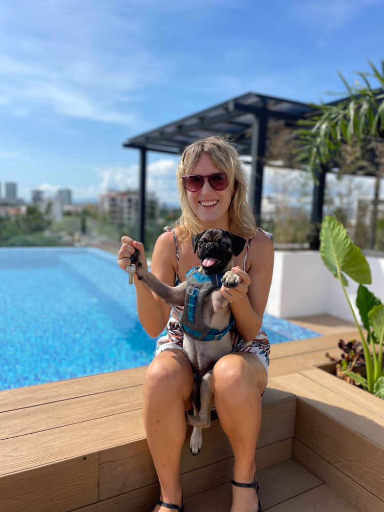 A woman holding a pug in front of a pool.
